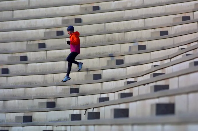 An athlete running down steps of an empty stadium.