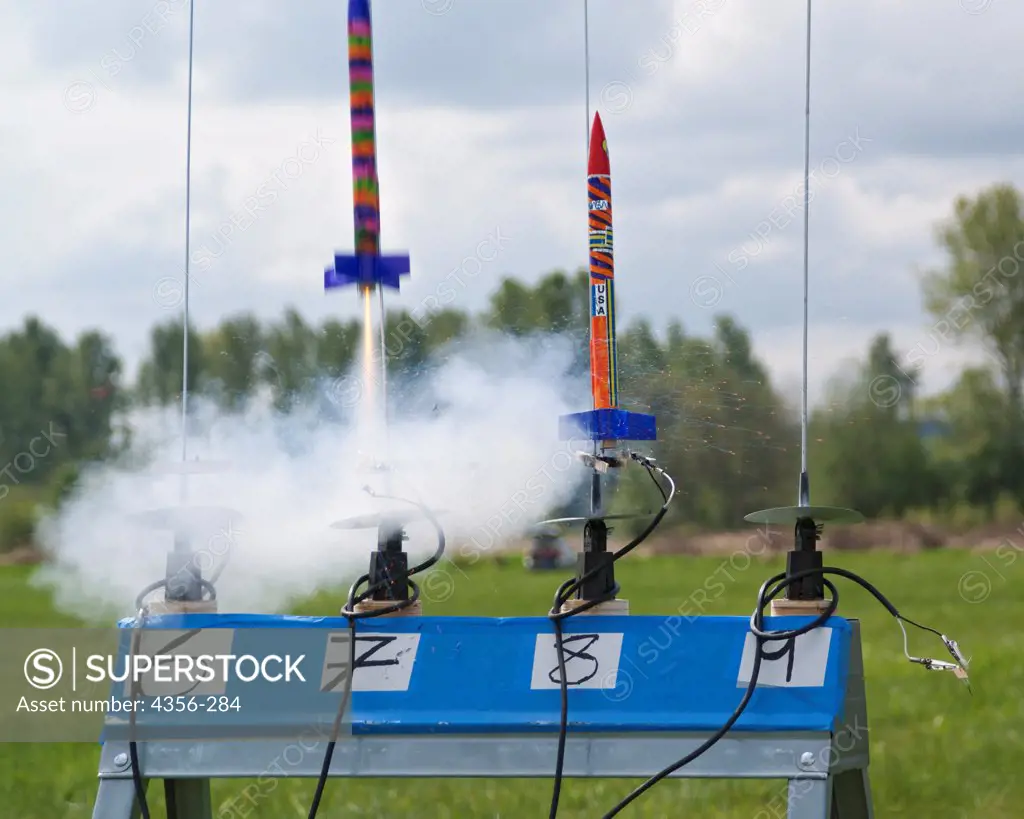 A row of brightly painted model rockets launch at a rocketry launch event.