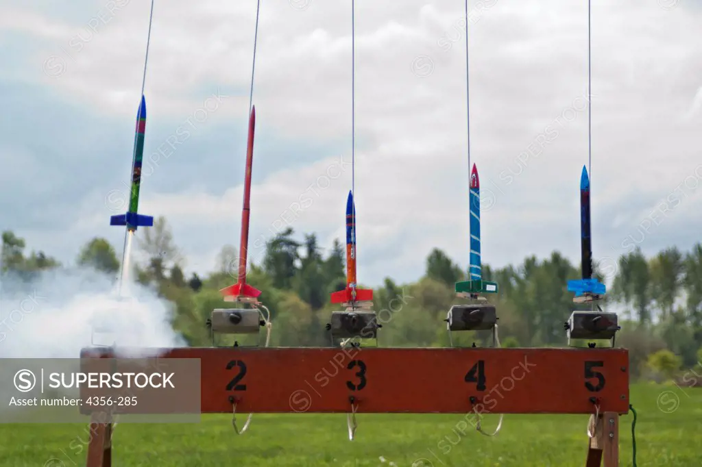 A row of brightly painted model rockets launch at a rocketry launch event.