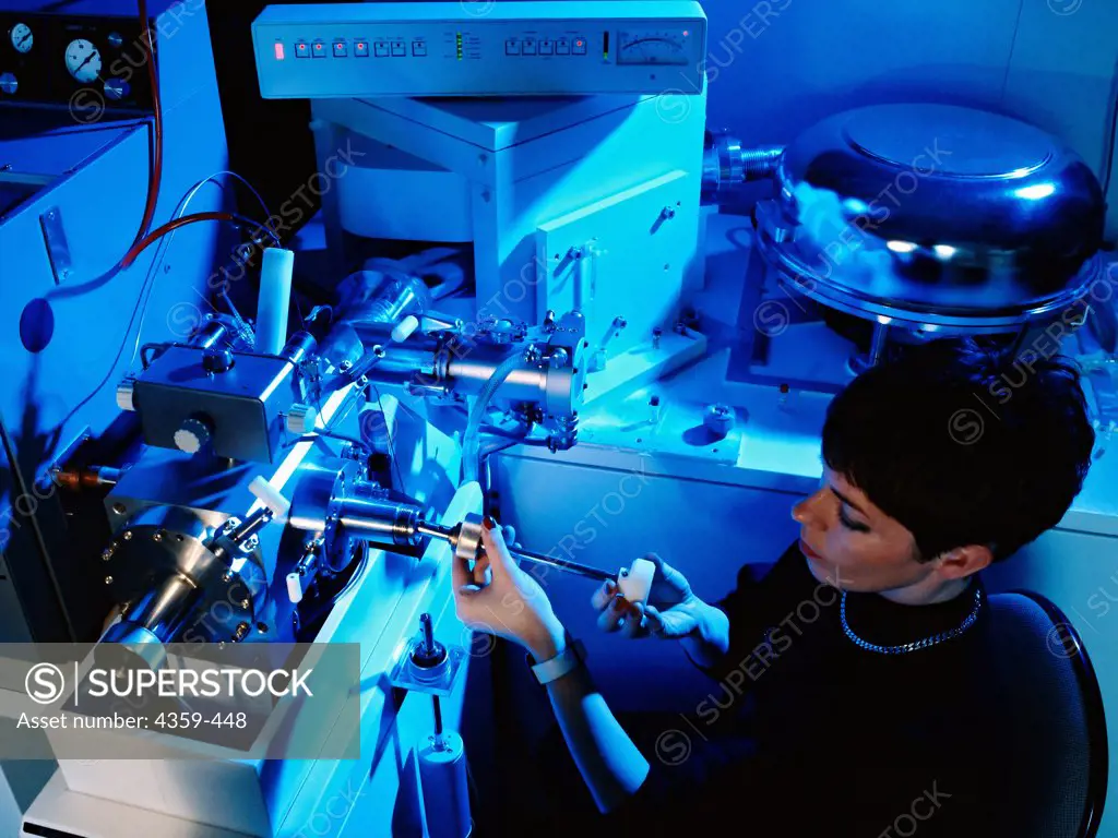 A laboratory assistant inserts a sample in a mass spectrometer for a mass spectrometry reading.