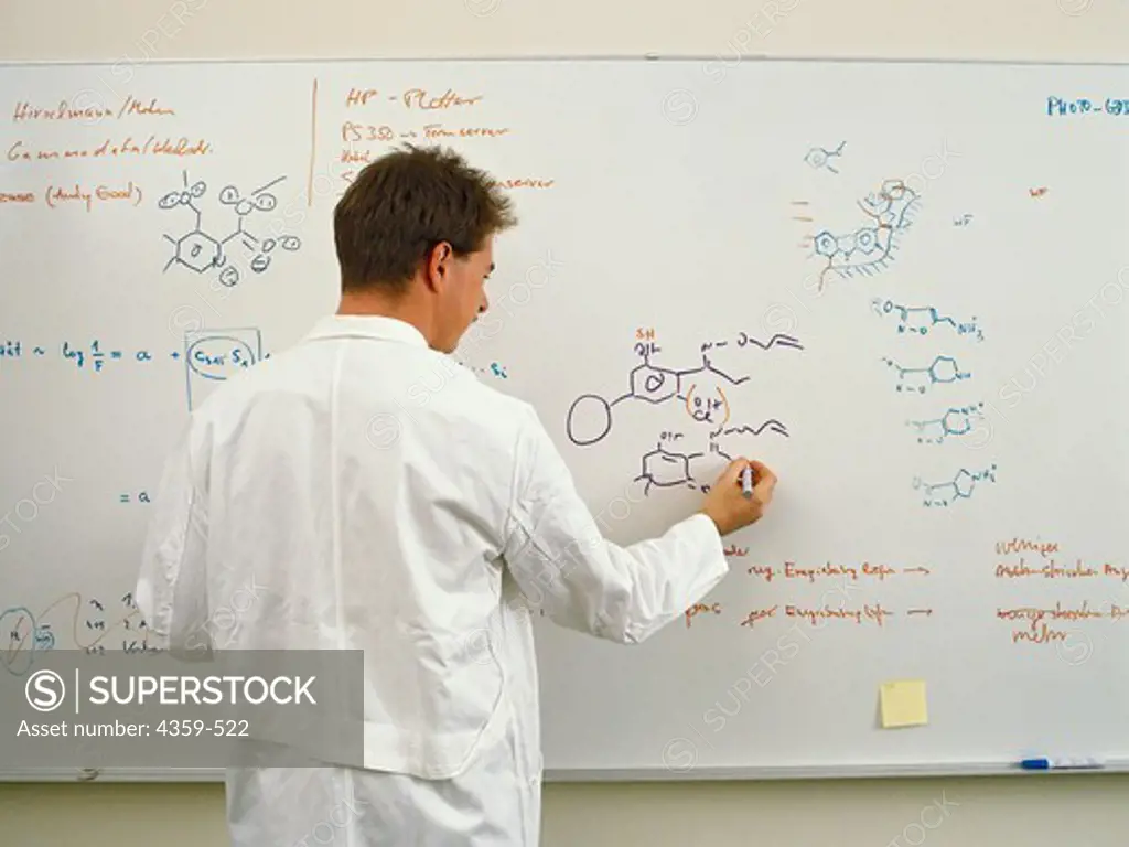 A scientist at a white board writing  molecular diagrams about drug research.