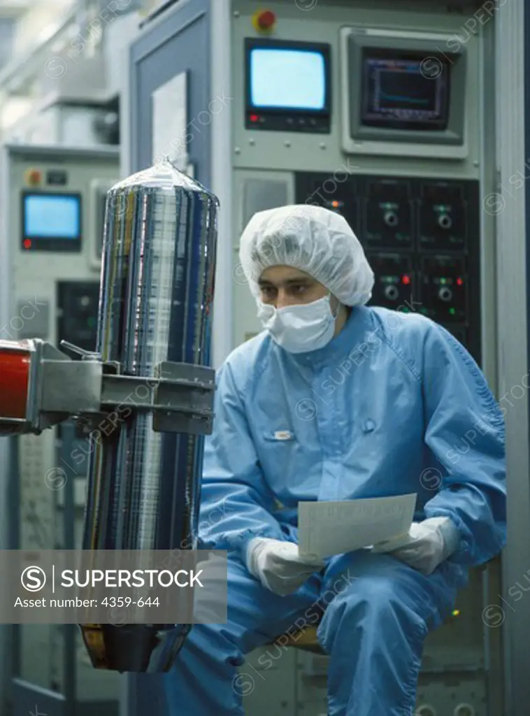 Worker wearing protective clothing inspects a bar of silicon crystal