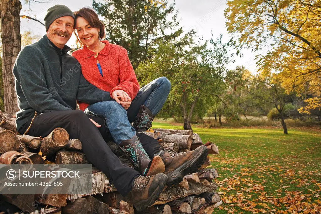 A couple sitting on pile of split firewood, in front of an apple tree in fall in northern New Hampshire, USA.