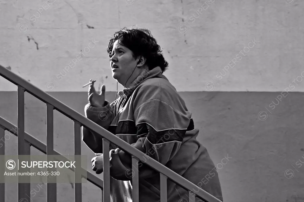 An overweight woman climbs stairs while smoking a cigarette.