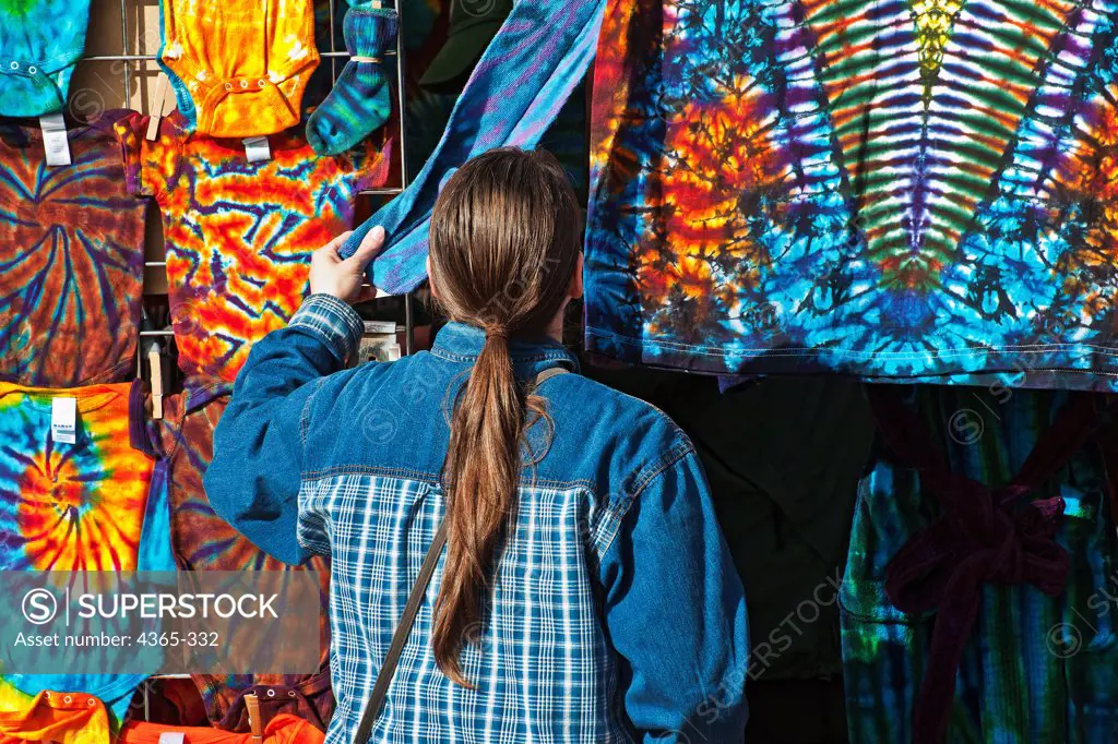 A ponytailed customer examines a tie-dyed t-shirt.