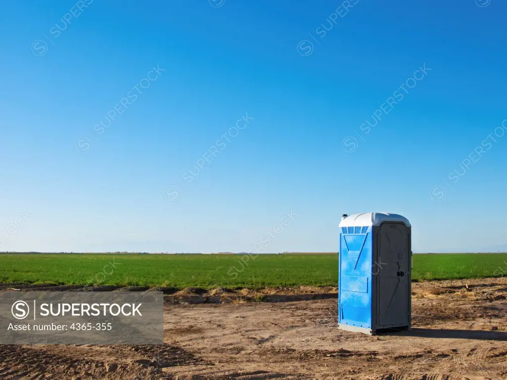 A blue portable toilet sits beside a large green field.