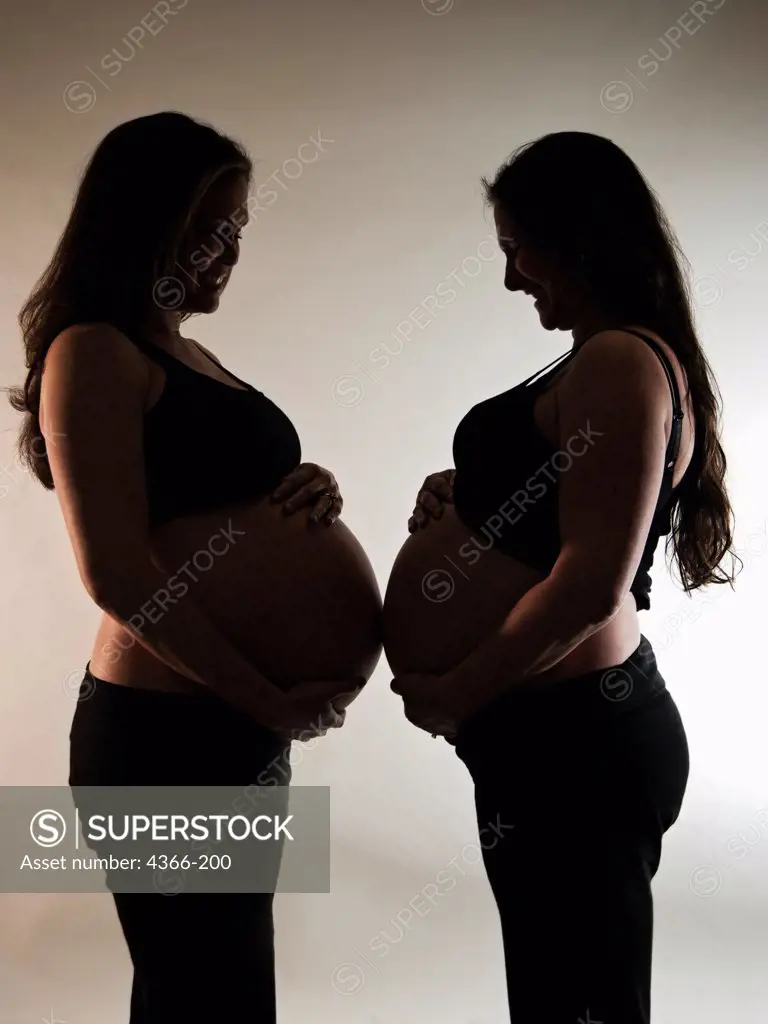 Two pregnant women face each other. The woman on the left is pregnant with twins. The woman on the right gave birth 13 hours after the picture was taken.