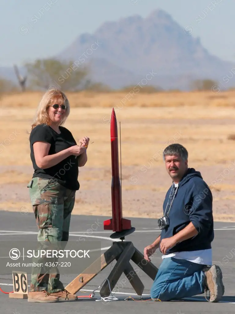 Larry and Sue Johnson prepare a red rocket for launch on a launch pad at a launch event sponsored by the Southern Arizona Rocketry Association (SARA).