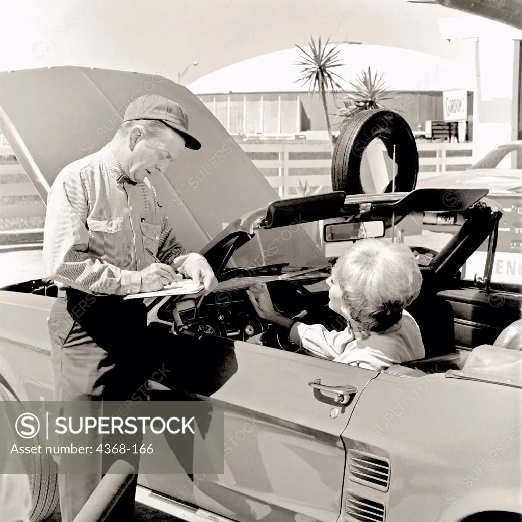 An ENCO service station attendant checks under the hood of a Ford Mustang for his customer.  The Houston Astrodome is in the background.  ENCO was subsidiary of Humble Oil; both were eventually folded into Exxon.