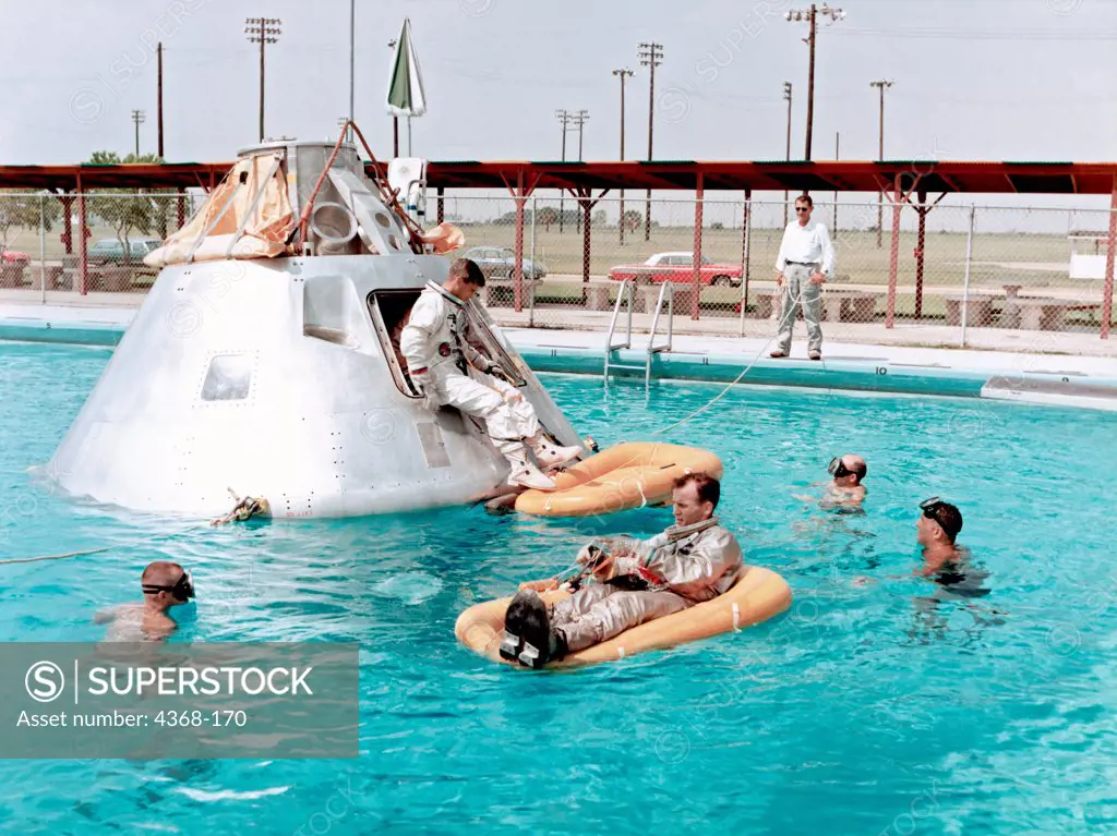 Prime crew for the first manned Apollo mission practice water egress procedures with full scale boilerplate model of their spacecraft. Astronaut Edward H. White II rides life raft in the foreground. Astronaut Roger B. Chaffee sits in hatch of the boilerplate model of the spacecraft. Astronaut Virgil I. Grissom, third member of the crew, waits inside the spacecraft.
