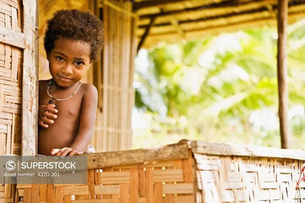 A young child peering out from a porch of a hut at Kofure Village, Oro Province, Papua New Guinea.