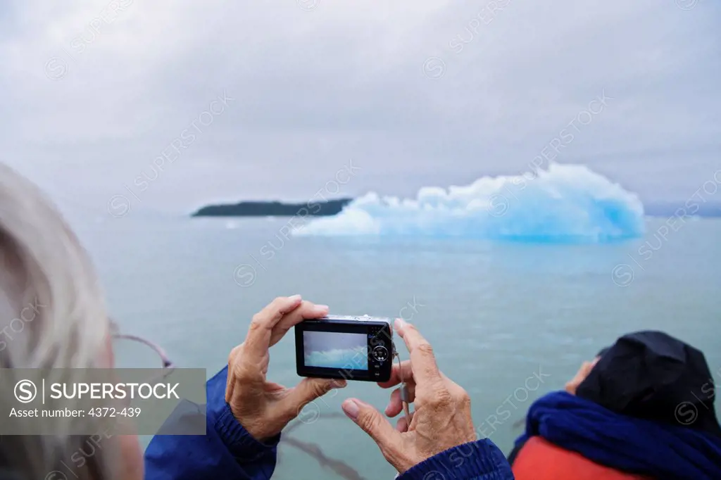 A sightseeing senior woman with a digital camera photographs ice from Le Conte Glacier, the southernmost tidewater glacier in the United States, near Petersburg, South East Alaska, on the Inside Passage.