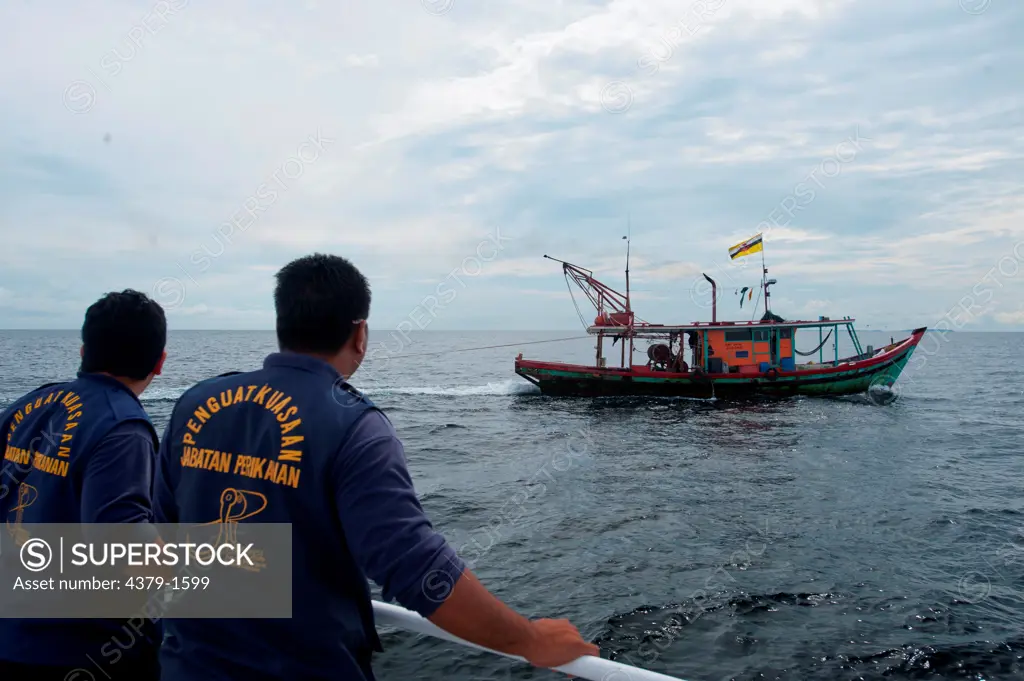 Fisheries department officials pull up next to a trawler hauling net to conduct a spot check, Brunei