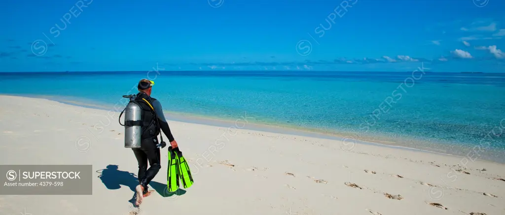 A diver walking to the water from beach, on North Huvadhu Atoll, The Maldives.