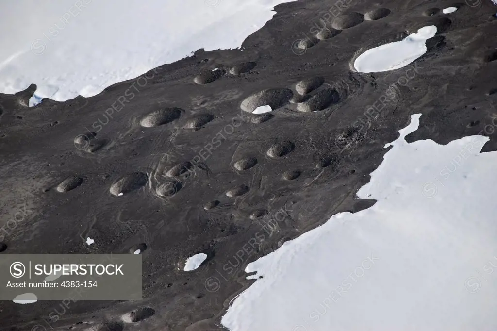 Crater-like pits in a deposit of material from pyroclastic flow on Mount Redoubt were caused by hot rocks. The rocks melted the snow and ice under the lighter flow material and fell into the snowbank. Image by Kate Bull for the Alaska Volcano Observatory/U.S. Geological Survey.