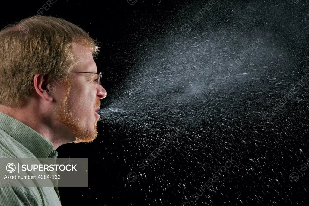 A sneeze in progress, revealing the plume of salivary droplets as they are expelled in a large cone-shaped array from this mans open mouth, dramatically illustrating the reason one needs to cover his/her mouth when coughing, or sneezing, in order to protect others from germ exposure. Illnesses like the flu (influenza) and colds are caused by viruses that infect the nose, throat, and lungs. The flu and colds usually spread from person to person when an infected person coughs or sneezes. Photo by