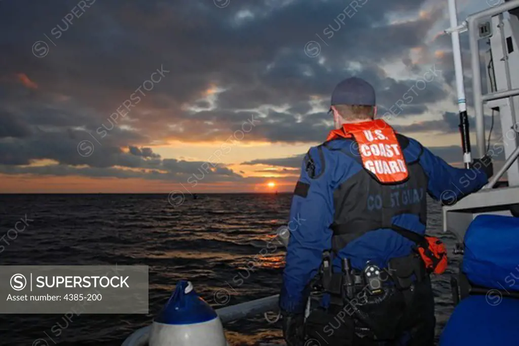 As the last moments of daylight illuminate the horizon, Coast Guard Petty Officer 2nd Class Eric Eberl, a boarding team member from Sector Boston, scans the sea for fishing vessels in Gloucester, Massachusetts. Teams from Sector Boston and Station Gloucester inspected fishing boats in Gloucester to ensure they were equipped with proper safety gear. (Coast Guard photo/Petty Officer 3rd Class Connie Terrell)