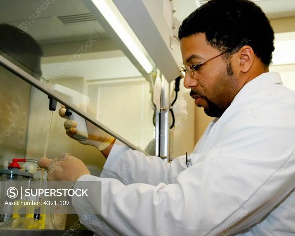 A scientist performs pipetting activities under a laminar flow hood. The hood filters the air and prevents contamination of the materials being worked with.  Photo by Diane A. Reid.