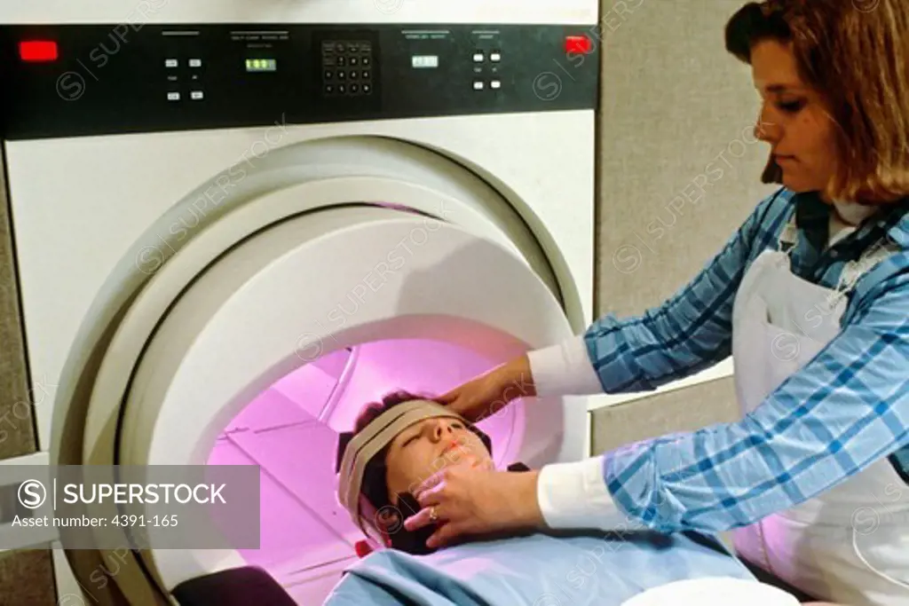 A woman's head is being secured by a female technician, preparing the woman for magnetic resonance imaging (MRI).