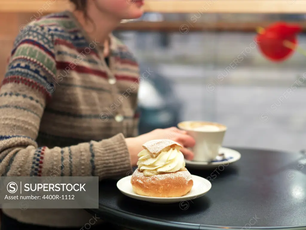 Young woman eating a piece of pastry at a cafe, Sweden.