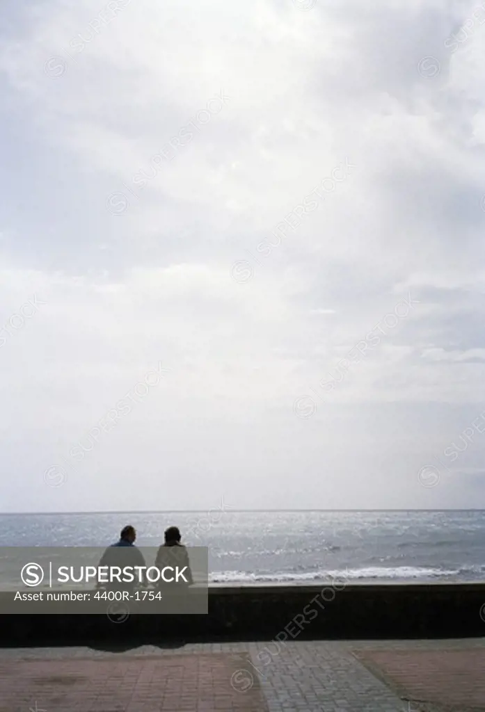 A couple sitting on a wall by the ocean, Meloneras, The Canary Islands Spain.