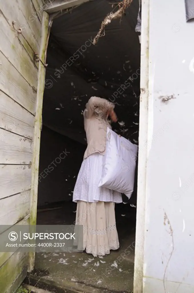 A young woman throwing down from a down pillow in an old house.