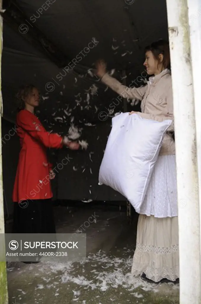 Two young women throwing down from a down pillow in an old house.