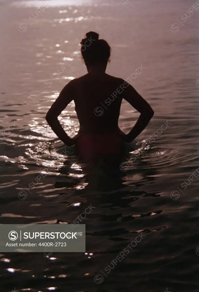 Woman standing in the sea at sunset, Sweden.