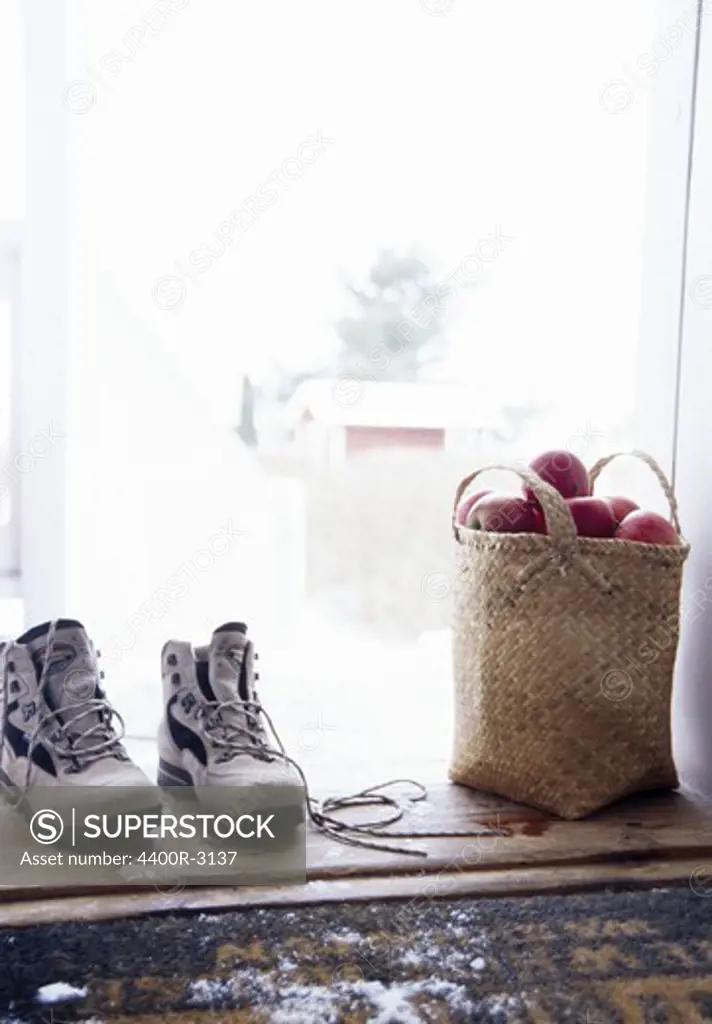 Pair of hiking boots and basket full of apples in doorstep