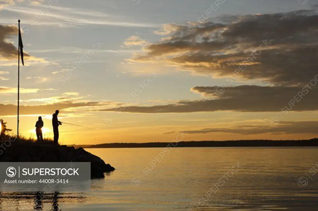 Silhouette of two persons fishing in the sunset, Sweden.
