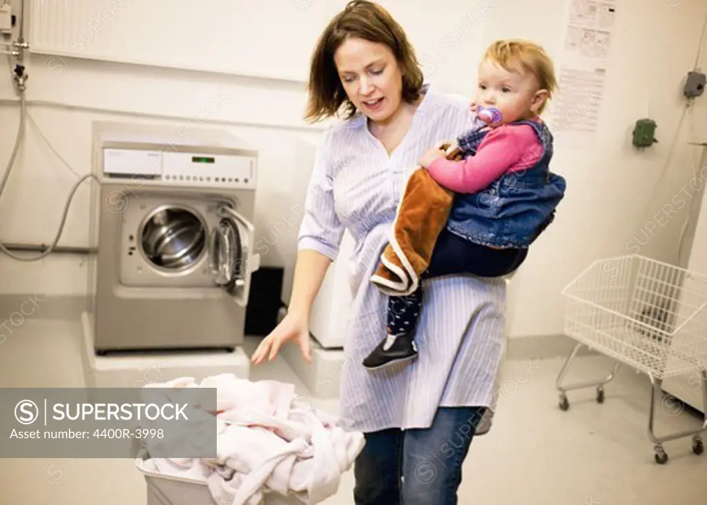Woman doing the laundry with her baby daughter, Sweden.