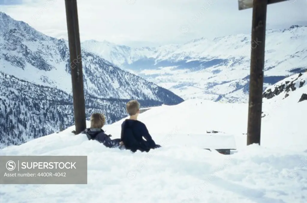 Two boys sitting in the snow up on a mountain, Italy.