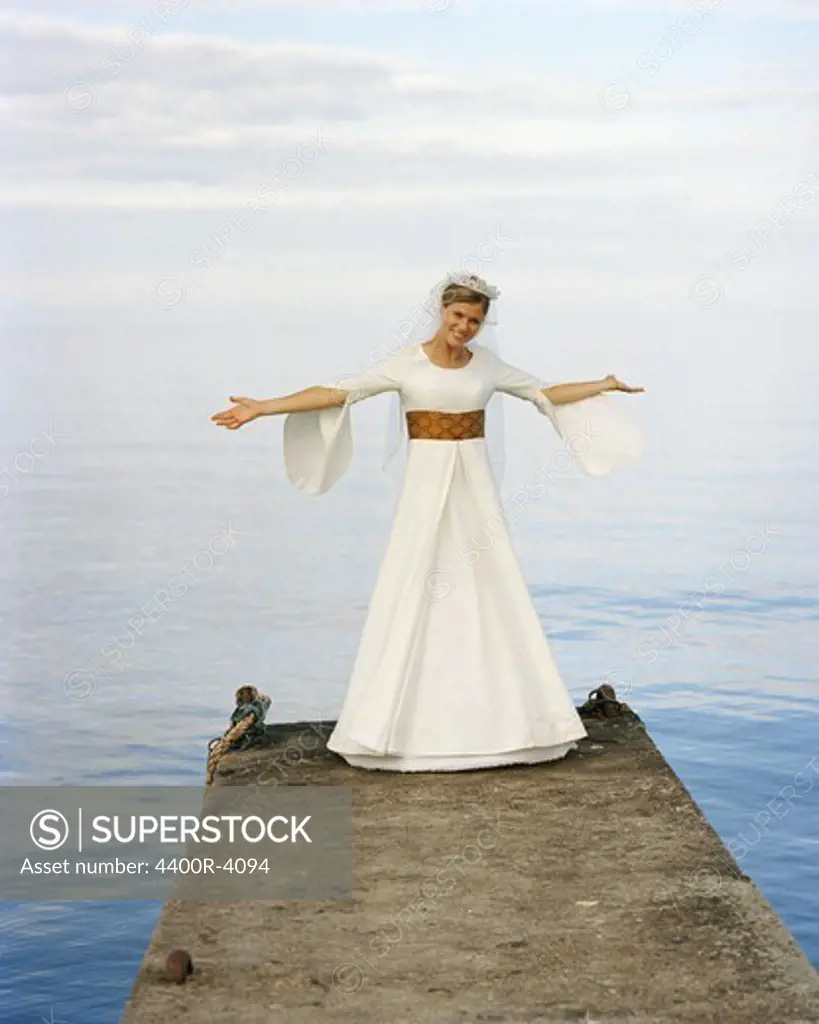 Scandinavia, Sweden, Oland, Bride standing on jetty arms outstretched, smiling, portrait