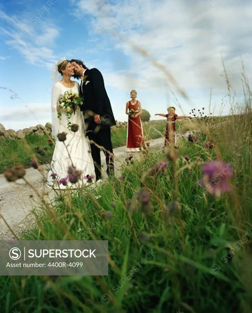 Scandinavia, Sweden, Oland, Bride and groom kissing with bridesmaid and flower girl in background