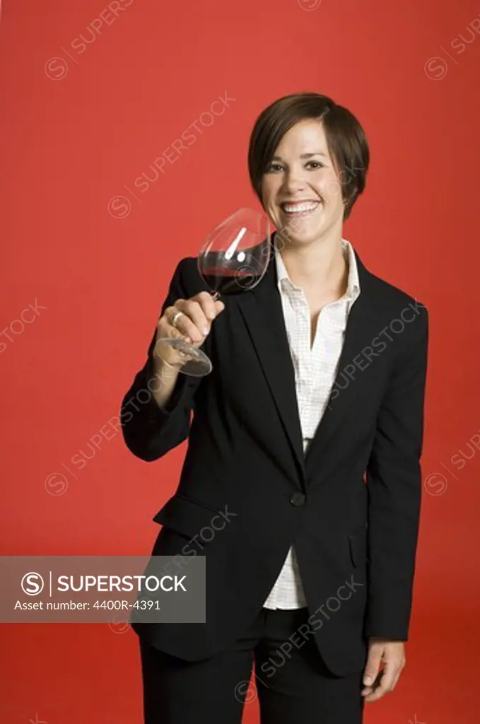 Female sommelier tasting wine against red background, smiling, portrait