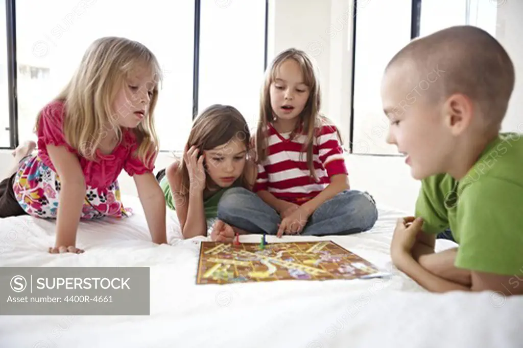 Children playing snakes and ladder on bed