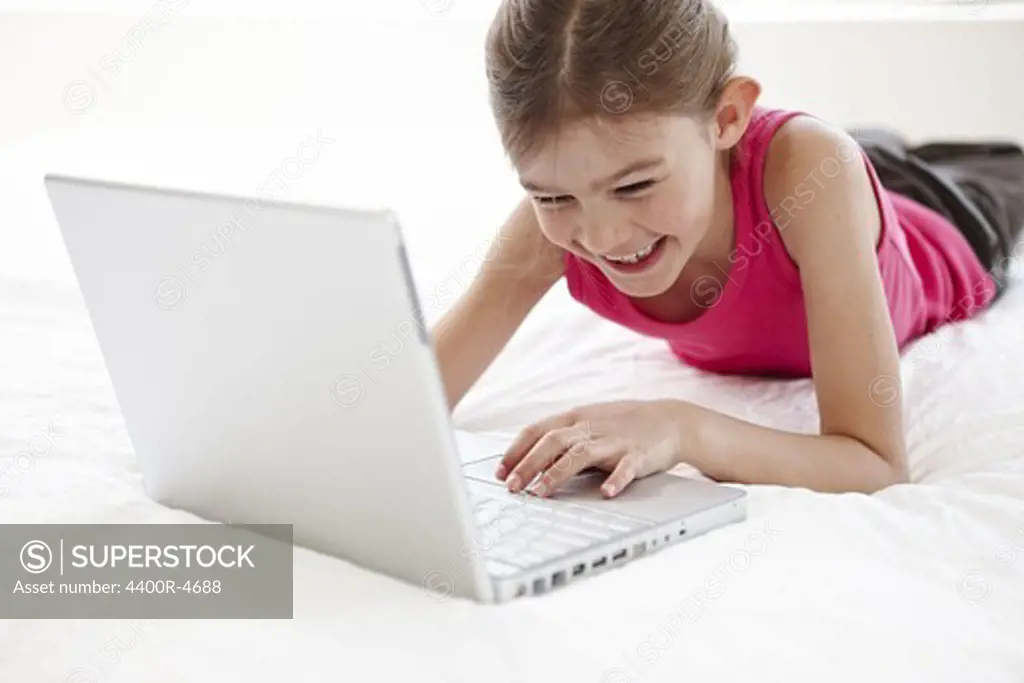 Girl using laptop on bed, smiling