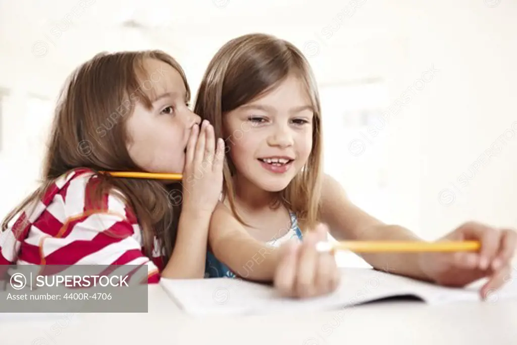 Girls whispering into each others ears while doing homework