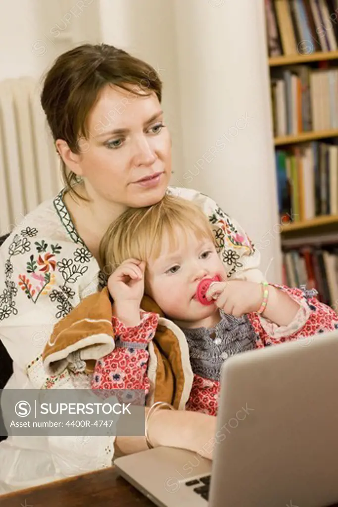 Woman using laptop with daughter on lap