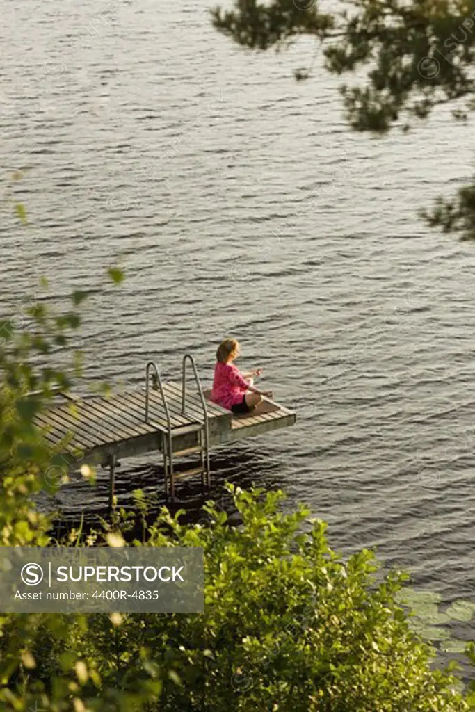 Woman meditating on jetty beside lake