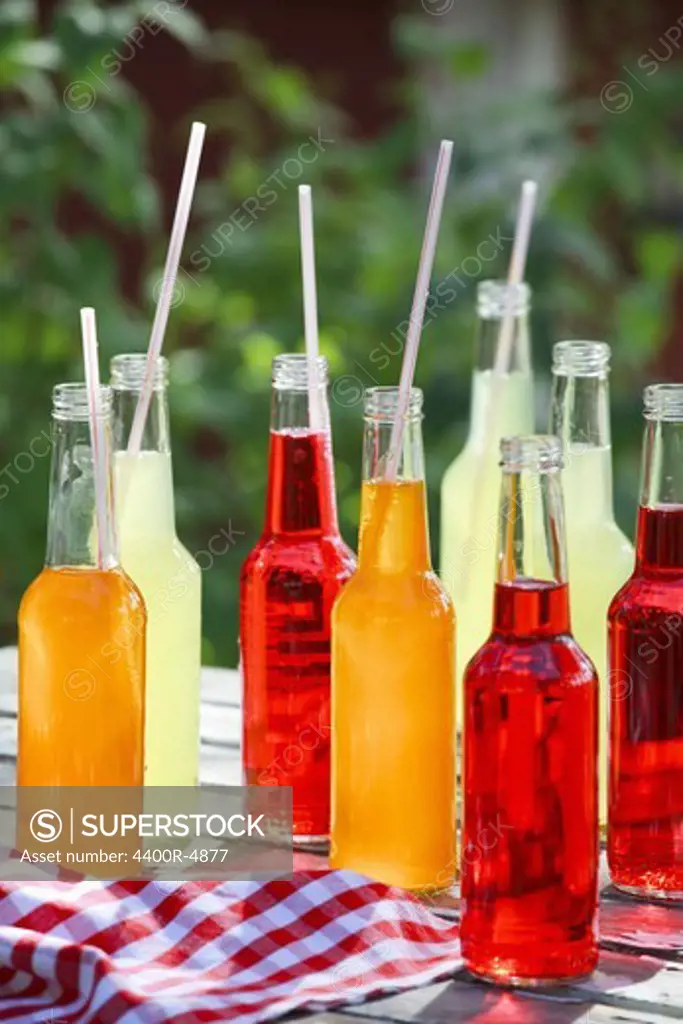 Bottles of cold drink with drinking straws on table, close-up