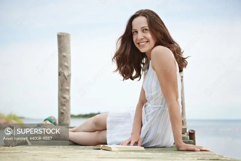 Woman sitting on jetty with book, smiling