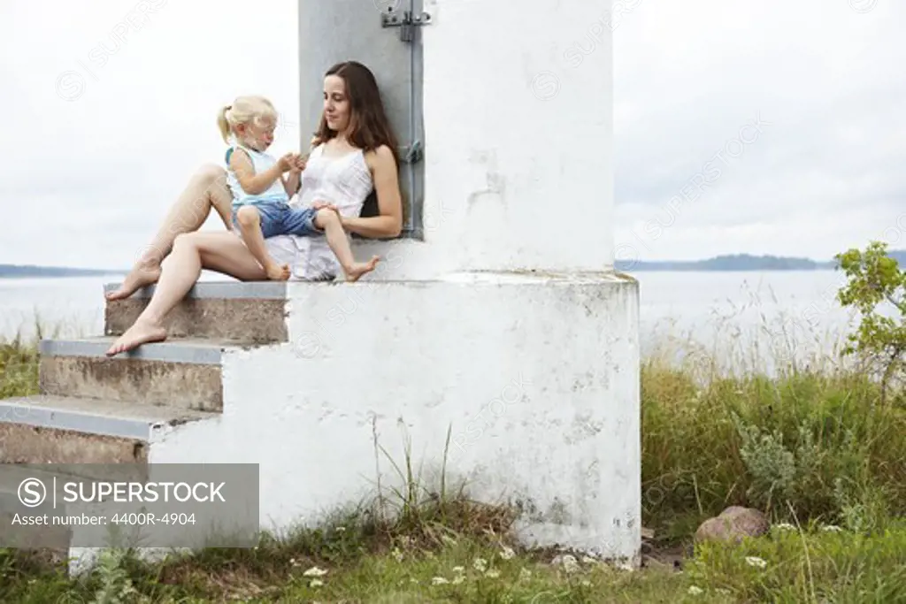 Mother and daughter on steps beside sea
