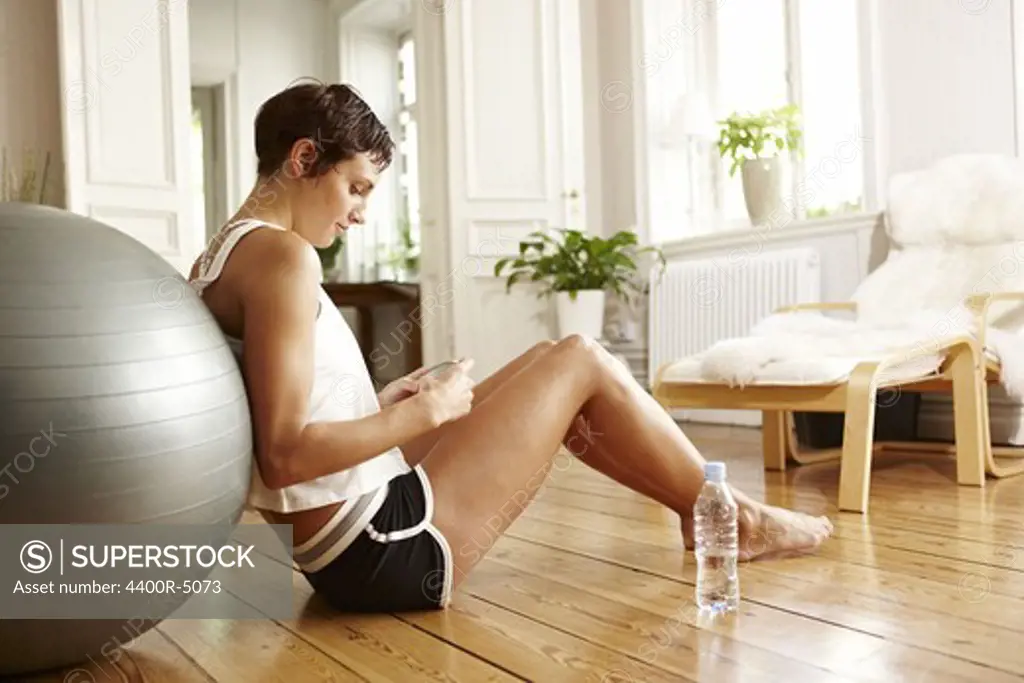 Young woman leaning on fitness ball holding phone