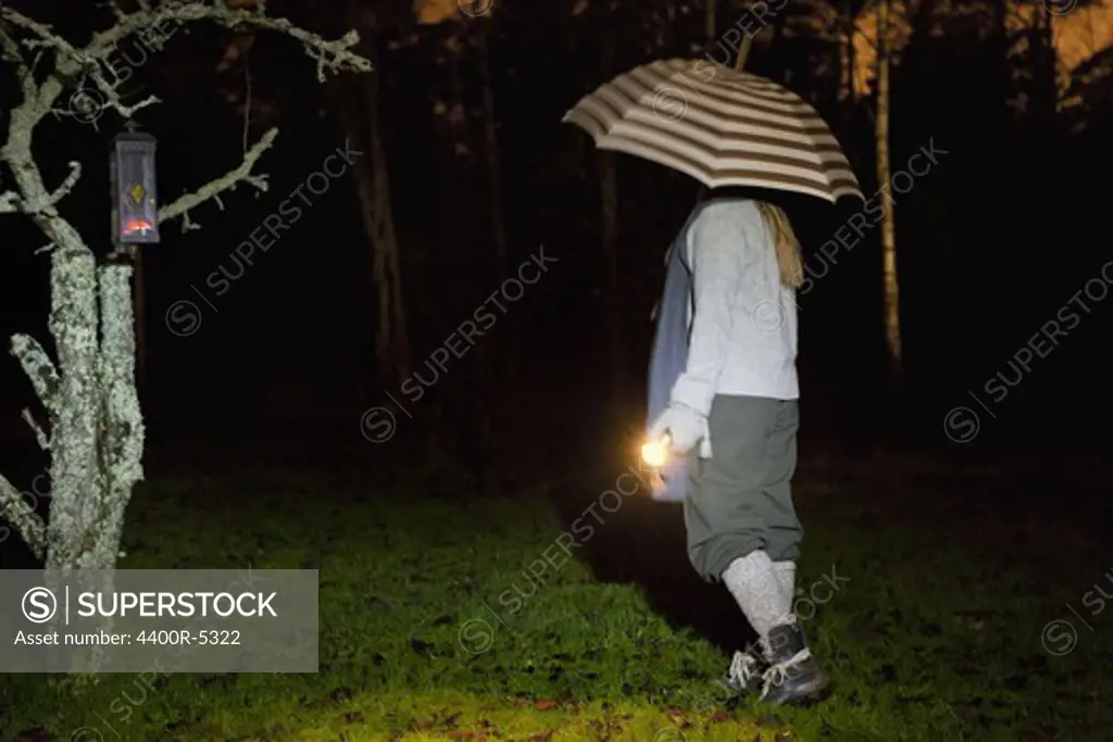 Girl with umbrella and torch walking in rain at night