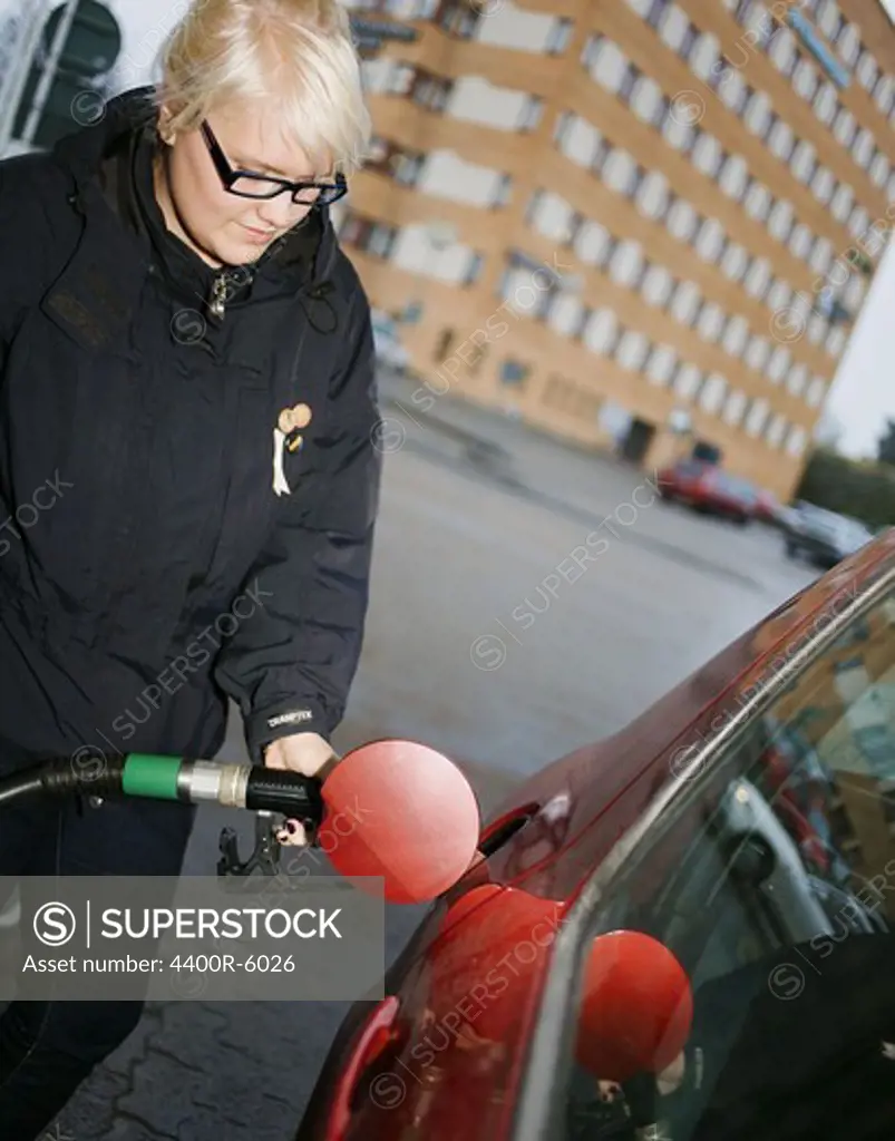 A young Scandinavian woman filling up the tank of a car, Sweden.