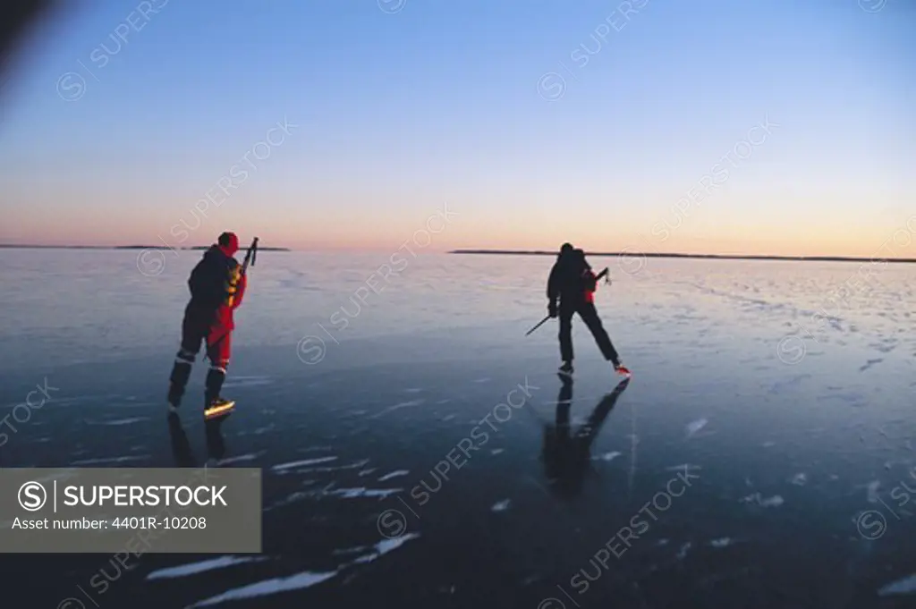 Two people skating on a lake at sunset, Sweden.