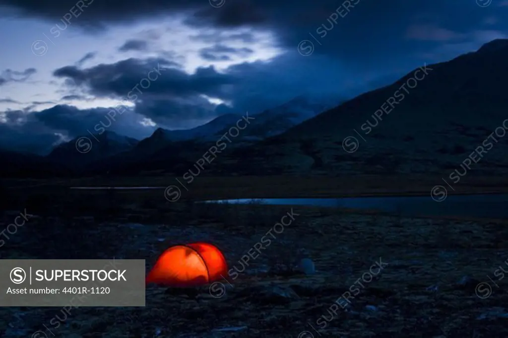 A well-lit red tent at a fjeld massif, Rondane National Park, Norway.