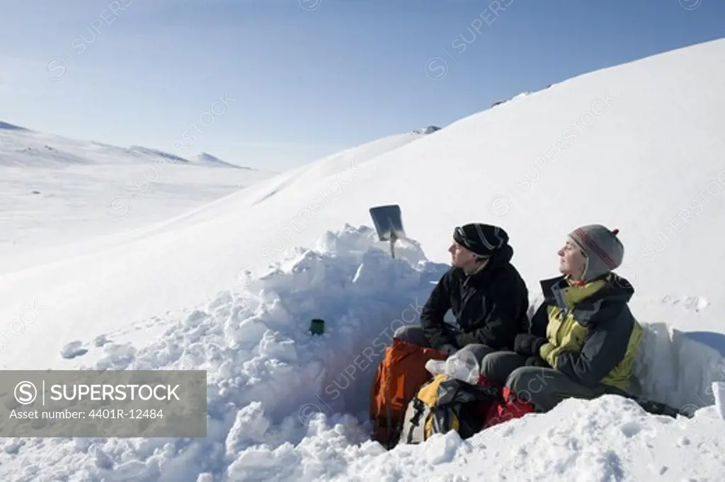 Couple resting on snow covered hill