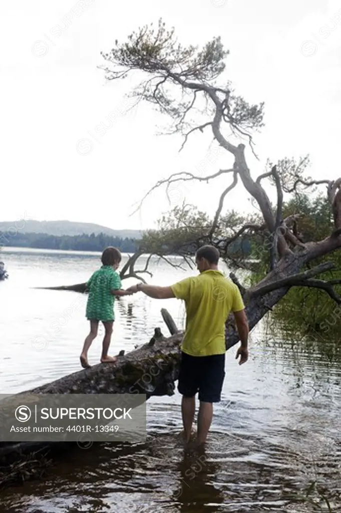 Father assisting son in walking on slanted tree trunk